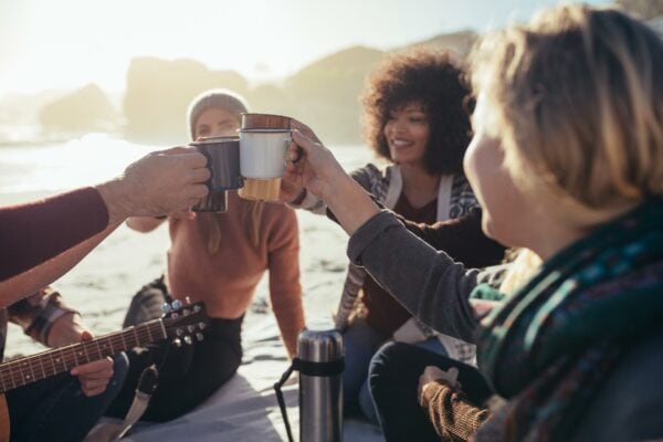 Eine Gruppe von Freunden stößt mit Kaffeetassen am Strand an.
